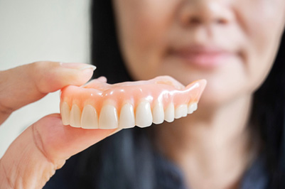 Woman holding complete upper arch of dentures to foreground