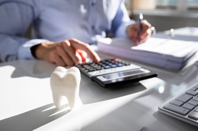 Man calculating with pen, paper, and calculator at desk with model tooth