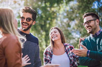 Four adults outside talking and laughing under trees on a sunny day