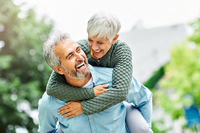 Woman in green sweater riding on the back of a man with a blue shirt outside smiling
