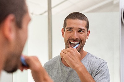 Man smiling while brushing his teeth in bathroom