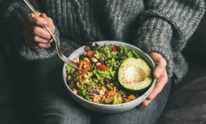 Woman in a grey sweater holding a fork and a bowl of salad
