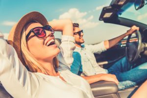 Woman and man driving under summer sun and smiling